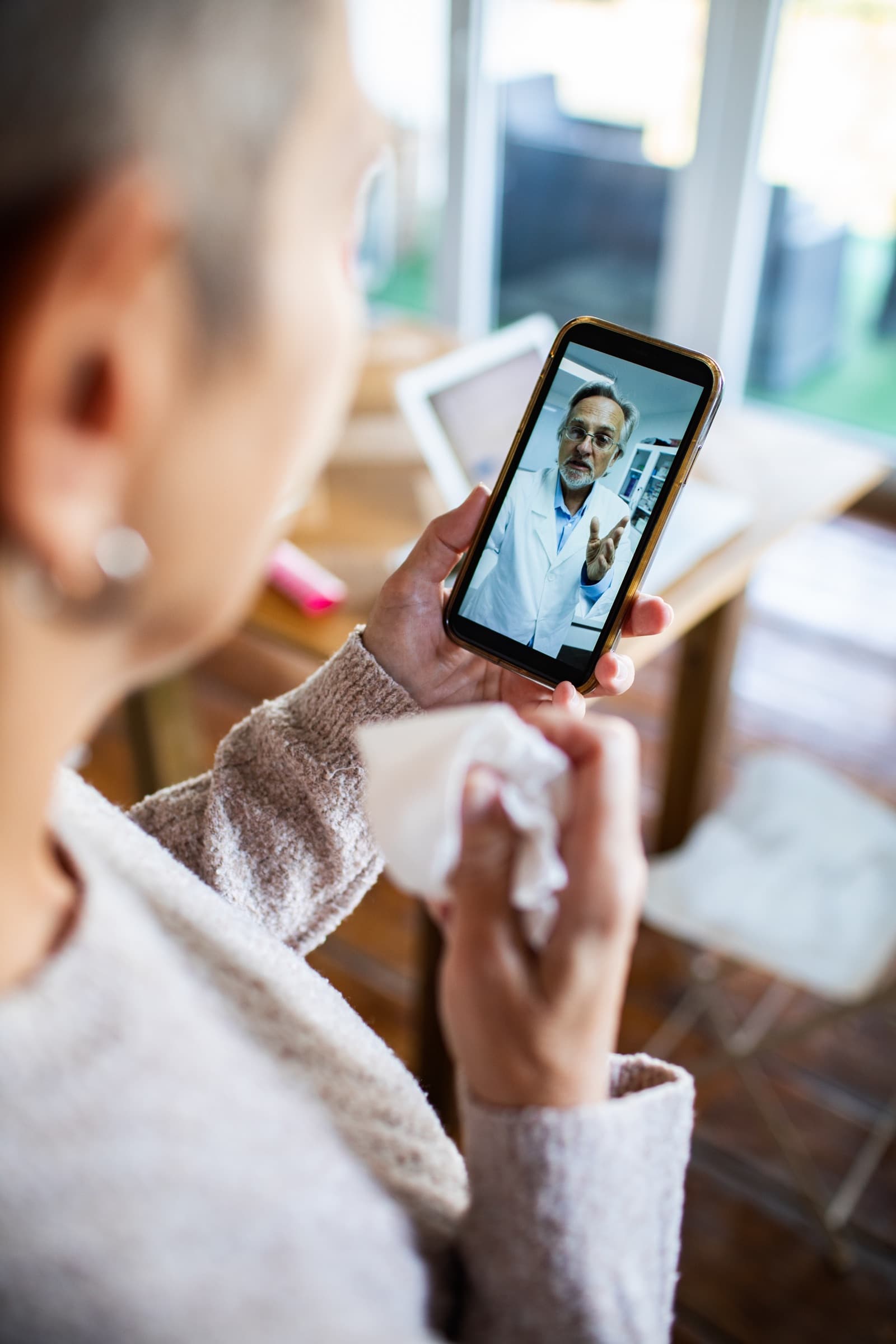 A woman on a video call with a doctor, holding a tissue