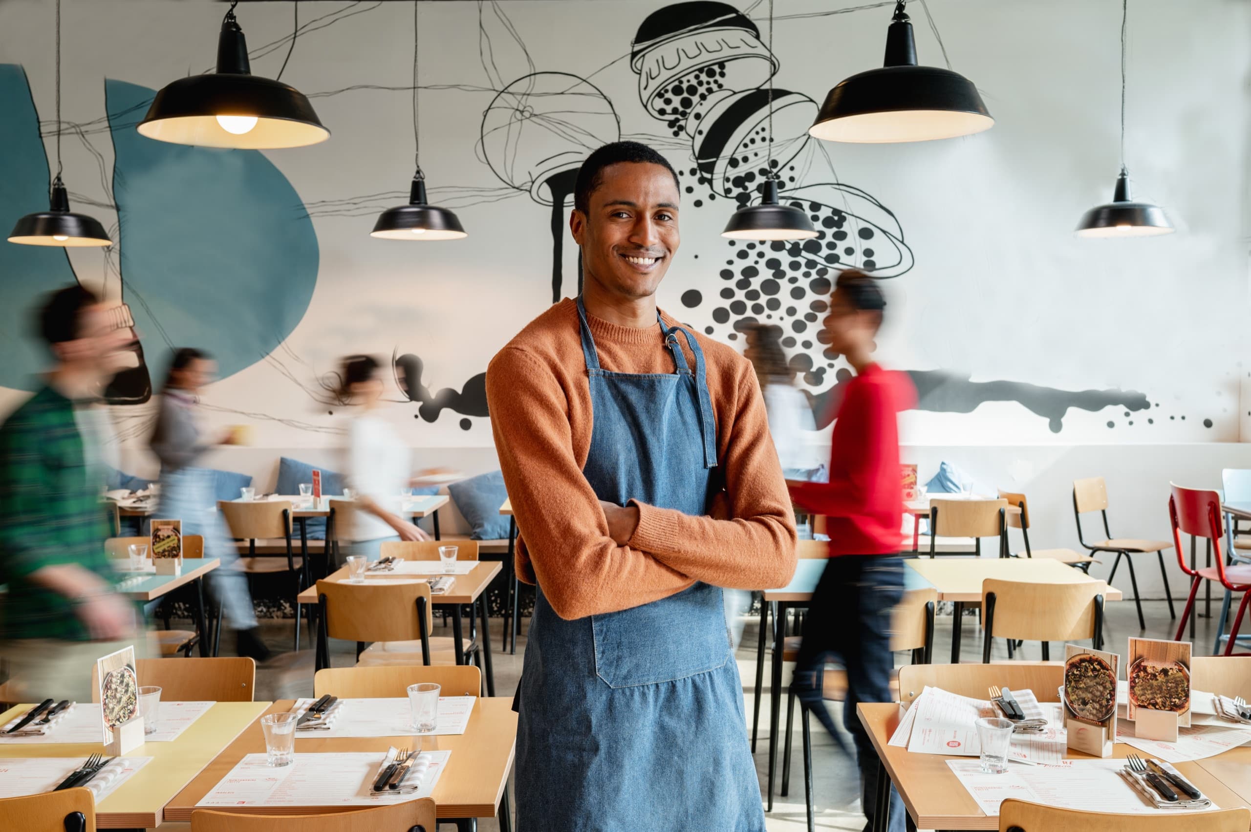 A smiling restaurant worker in an apron in a busy dining room