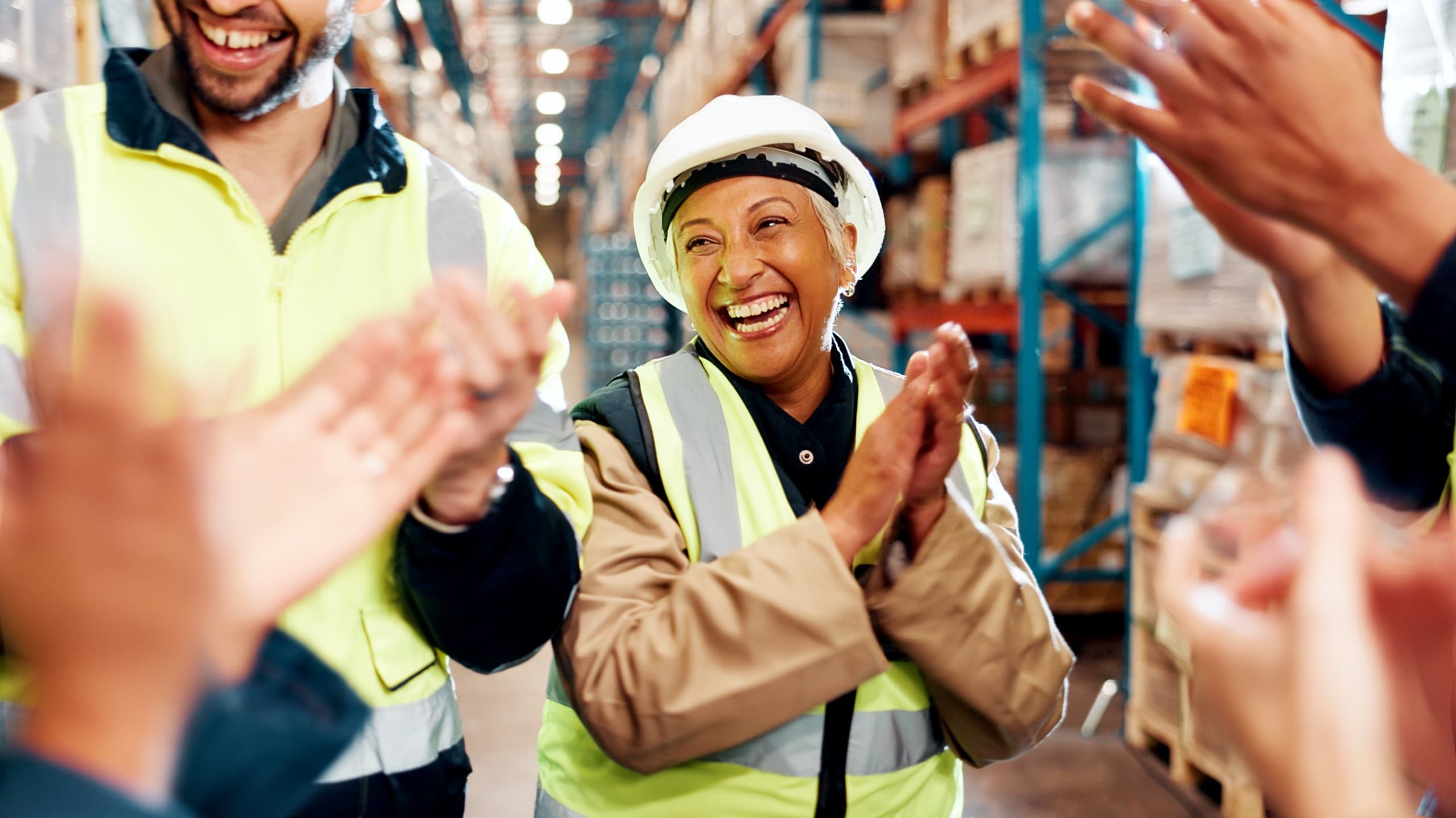 Warehouse workers in hard hats and safety vests applauding
